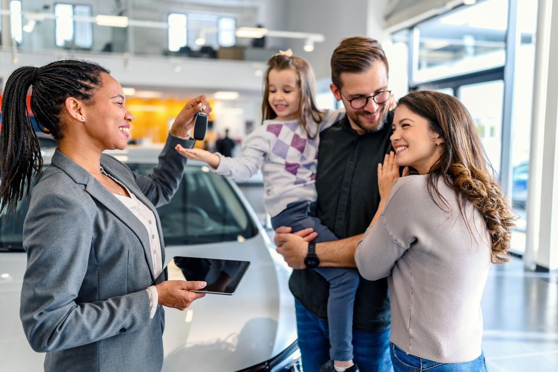 Sales person giving car key to family in car dealership