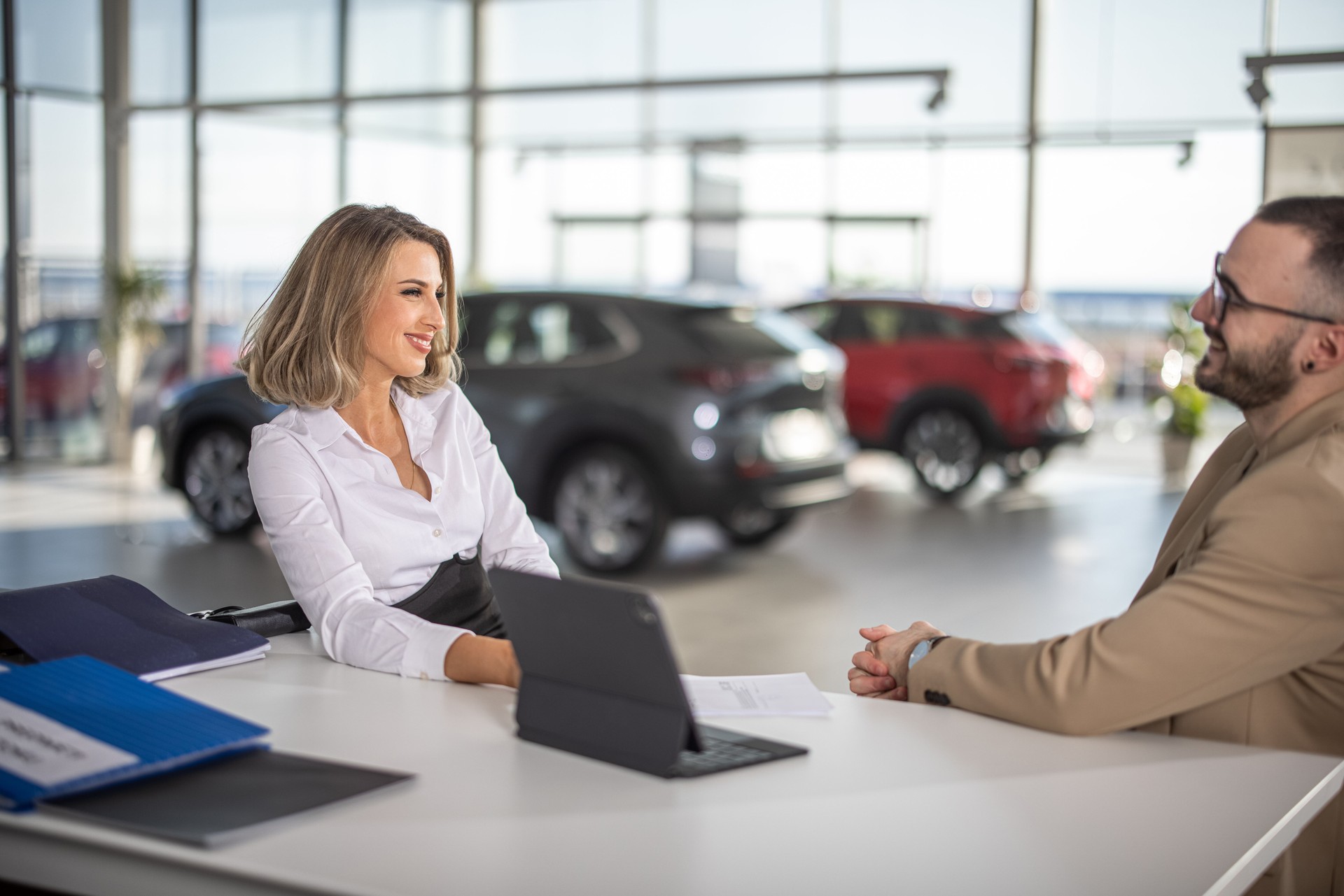 Sales woman sitting and talking with male customer in car dealership